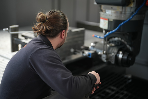 Rear view of blue-collar brown-haired man working on CNC machine in industry