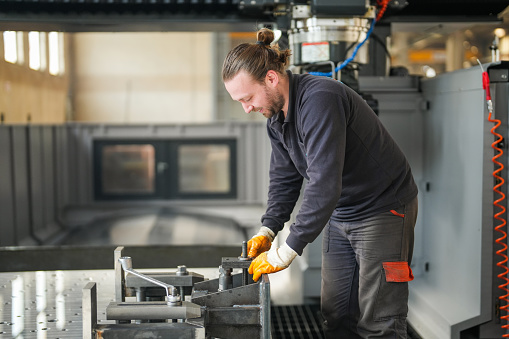 Male technician placing parts on CNC machine in industry