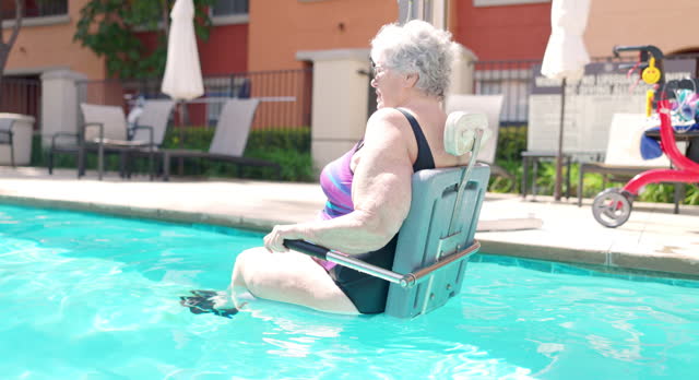 Senior woman using accesibiltiy pool lift chair to get out of pool