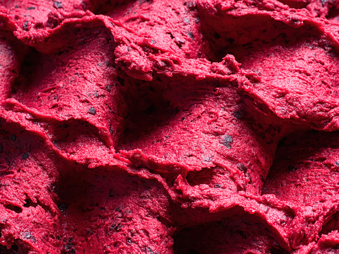 Frozen Black Currant flavour gelato - full frame detail of sorbet. Close up of a red surface texture of Ice cream filled with pieces of mixed fruit.