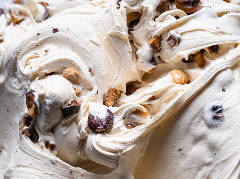 Frozen hazelnut flavour gelato - full frame detail. Close up of white creamy surface texture of Ice cream filled with pieces of nuts.
