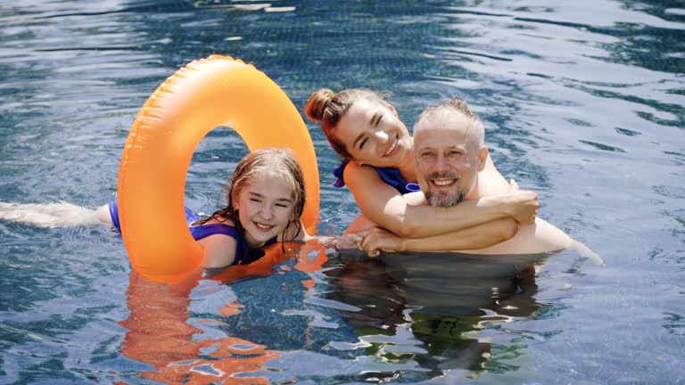 Girl lounges in pool on inflatable ring. Happy kid with family spend summer vacation on inflatable ring on pool. Concept: enjoy moments of poolside calm with inflatable ring