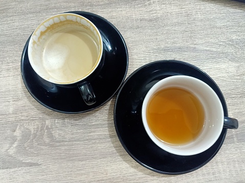 Two glasses containing tea and cappuccino on a wooden table