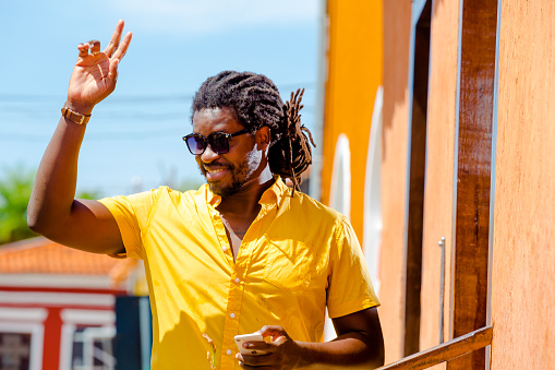 handsome black man wears yellow shirt, sunglasses and afro hair. waves to someone out of frame