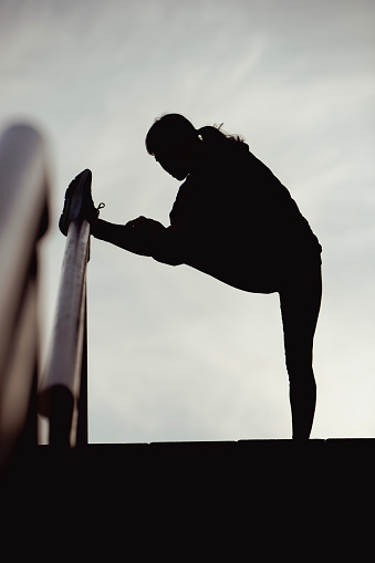 High Contrast Silhouette Portrait of Sports Woman Runner Warming Up Before Run Outdoors in the City
