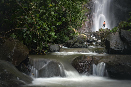 Solitary male traveller at the famous scenic Yeh Mampeh waterfall flowing in the tropical forest of Buleleng province, Bali island, Indoneisa