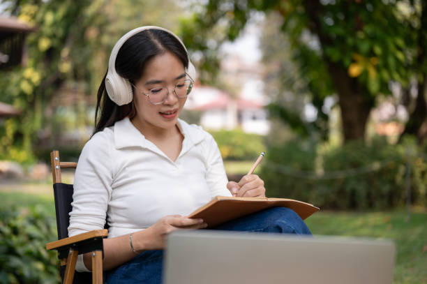 istock A young Asian woman is focusing on writing her work or keeping a diary while sitting in a backyard. 2077061377