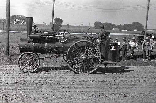 Cedar Falls, Iowa, USA - August 23, 1958: Advance Thresher Company steam traction engine being driven in the Threshermen's Field Days parade. A steam engine like this would have been used to power a threshing machine or other farm machinery. Although steam engines and steam tractors were used in the US until the late 1930s and early 40s, collector groups were already forming by the time this photo was taken in 1958 to preserve steam engines and tractors.