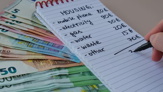 Female hand writing and Counting expenses bills on housing electricity, gas, water. Banknotes of euro cash around. High prices for energy inflation crisis. Cut back on spending