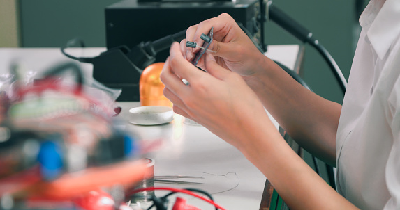A concentrated female technician skillfully solders electronic components on a circuit board in a technology laboratory setting.