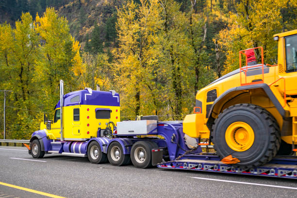 istock Blue and yellow powerful big rig semi truck transporting oversize load on heavy duty step deck semi trailer driving on the autumn highway road 2077226806
