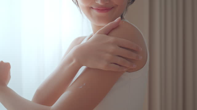 Happy young asian woman applying body lotion and skincare cream on arm, Beauty skin concept