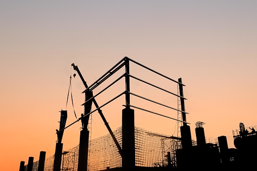 Silhouette of construction workers installing steel roof structure of a warehouse with sunset background. Civil structural and erection work.