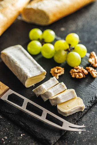 Detailed close-up of a cut Brie cheese accompanied by crisp grapes on a black slate surface, highlighting texture and form