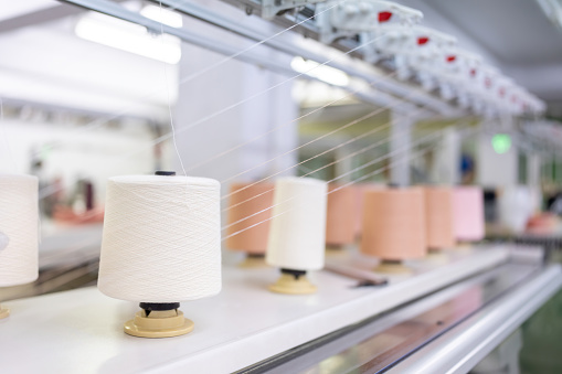 Large spools of white thread ready for use in sewing and making clothes in a weaving factory. Around there are sewing machines working. Waiting to be exported to department stores