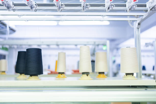 istock Rolls of white and black thread are lined up in rows on a large sewing machine in a weaving industry that uses computer technology to produce clothing and fabric for export to foreign markets. 2077397596