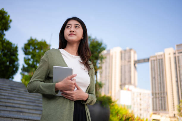 istock Young Asian woman holding digital tablet while walking in downtown district 2077400260