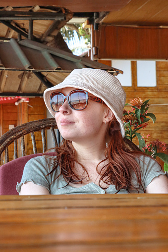 Stock photo showing close-up view of a beautiful, red haired young woman sitting in an al fresco wooden balcony on holiday.