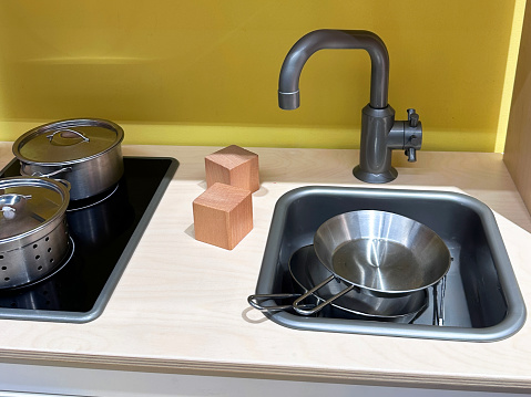 Stock photo showing an indoor play kitchen cabinet pretend stove hob, sink unit and oven with cooking pots and frying pans.