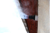 Water vapor from a gas central heating boiler flue condenses in cold air. The flue vents through the exterior wall of a building. Gas boiler chimney in winter time