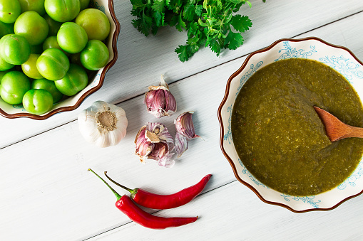 Tkemali sauce, traditional Georgian cuisine, green cherry plum, with ingredients for sauce, cilantro, mint, hot pepper, garlic, on a white wooden table, close-up, rustic, food background, no people, selective focus, sauce, green sauce, tkemali, georgian cuisine, homemade,