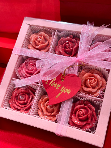 Stock photo showing close-up, elevated view of collection of red and pink wax candles in rose designs in a gift box with cellophane window.