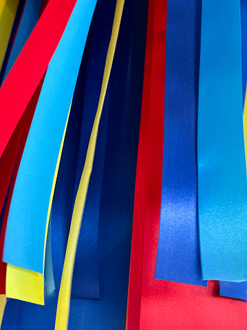 Stock photo showing close-up, low angle view of Christmas decoration made of hanging, multicoloured, satin ribbons in red, turquoise, light blue, dark blue and yellow.