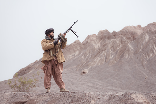 A Taliban soldier stands with a machine gun, In the desert mountain landscape