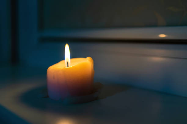 Burning candle standing on a windowsill late in the evening night.