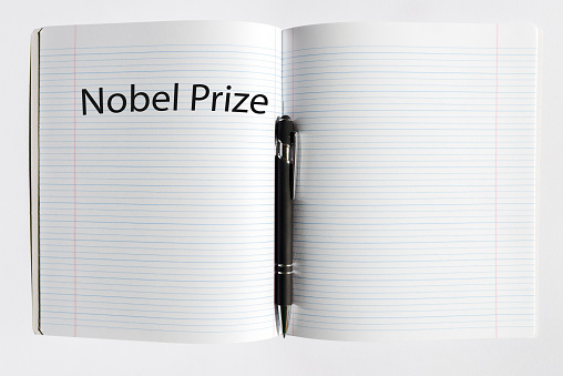 The inscription NOBEL PRIZE on a white sheet notebook.Nobel prize in literature. A pen is lying nearby.White background.Selective focus,close-up,copy space.