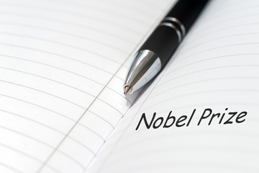 La inscripción NOBEL PRIZE en un cuaderno de hojas blancas. Premio Nobel de Literatura. Un bolígrafo está cerca. Fondo blanco. Enfoque selectivo, primer plano. photo