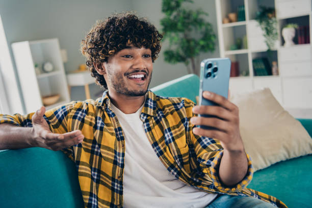istock Photo of cheerful handsome guy sit sofa communicate vlogging record video make selfie smart phone apartment indoors 2077575374