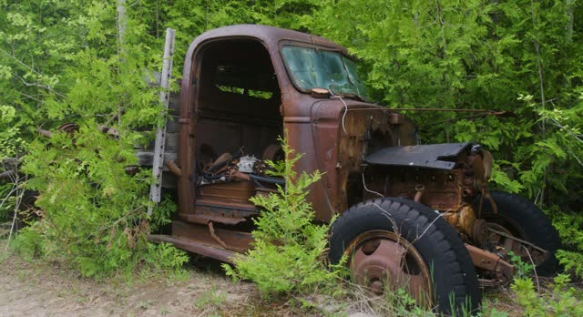 Panning shot showing the deserted road then an abandoned 1940s truck rusting away and overgrown with weeds and trees.