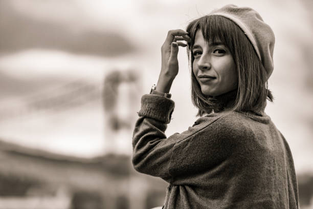 9-year-old girl girl with a patterned headscarf looks upward with an expression of wonder. She has short hair partially visible beneath the scarf and is photographed in a natural outdoor setting with foliage in the background. The image is captured on black and white film, creating a classic, timeless quality with rich contrast. The close-up portrait focuses on her face with soft natural lighting highlighting her features.