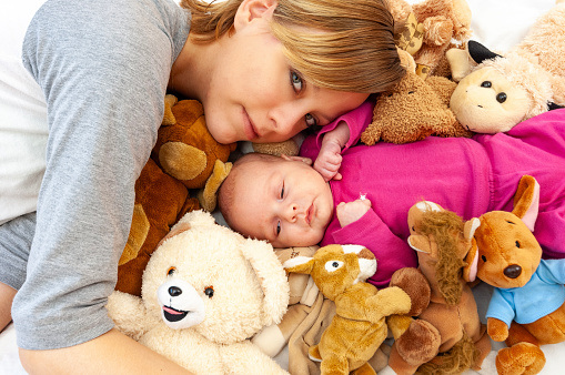 High angle view of mother and baby surrounded by baby toys, looking at camera.
