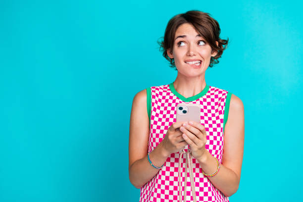 istock Portrait her nice young lady smartphone look empty space biting lips unsure do not remember login isolated on cyan color background 2077660997