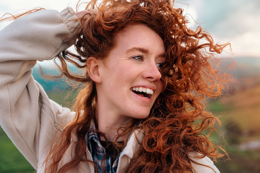 Close up of portraut of amazing redhead woman reaching the destination and enjoying mountains landscape on the top of mountain at sunset. A trip to the mountains with a backpack. Travel  Lifestyle