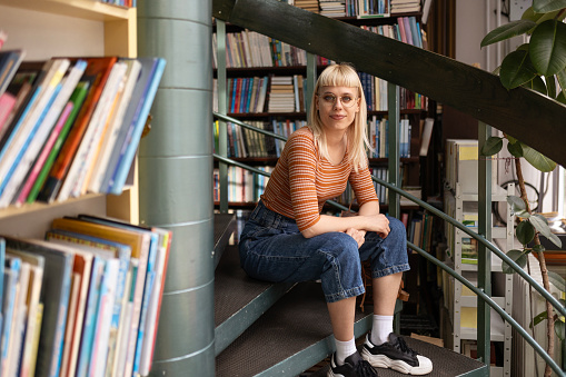 Female student in library sitting on staircase of library