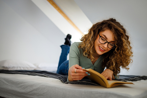 Smiling young lady reading a book while lying down in bed