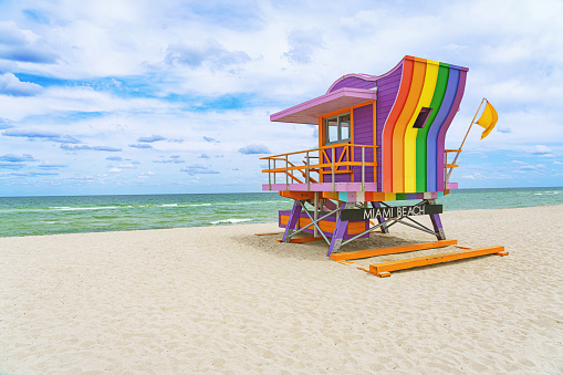 Vibrant, pastel view of lifeguard tower colorful painted as LGBT flag under bright blue sky on South Beach, Miami, Florida.