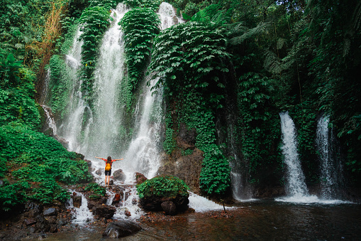 Woman  in red kimono standing near the refreshing waterfall on Bali