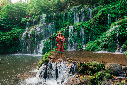 Woman  in red kimono standing near the refreshing waterfall on Bali