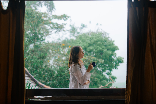Woman drinking coffee in the morning on tropical villa visible through the window