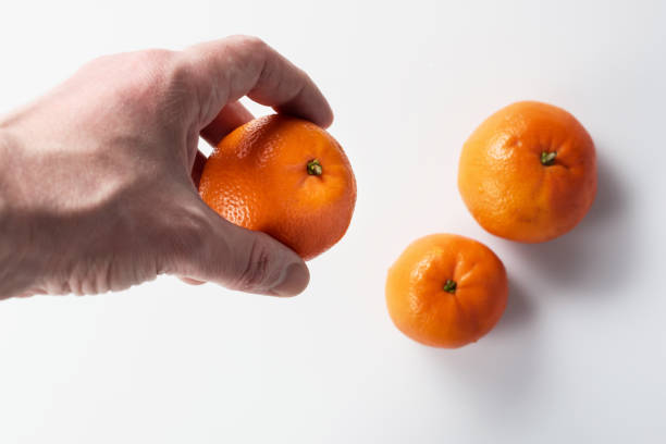 A man's hand holding a ripe tangerine or clementine against a background of other tangerines