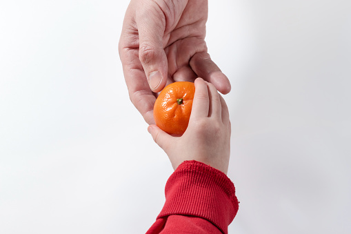A father gives his young daughter a ripe tangerine or clementine in close-up