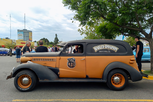 Buenos Aires, Argentina - Feb 25, 2024: Old aged brown 1938 Chevrolet Master delivery van with Harley Davidson logo and brand at a classic car show in a parking lot. Side view. People looking at the cars. Copy space.
