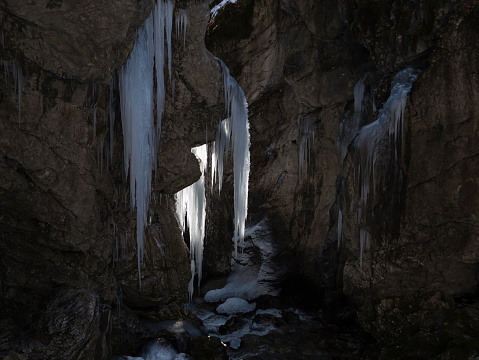 Wonderful contrast between the illuminated icicles and the dark shadowy gorge. Backlit ice formations created by the freezing of trickling water. Amazing creations of nature in cold winter season.
