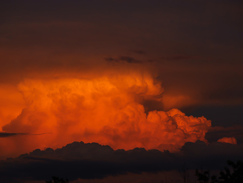 Majestic view of orange glowing cumulonimbus storm cloud forming on summer sky. Dramatic cloudscape developing over countryside. Threatening thunderclouds in gorgeous and vibrant sunset colours.