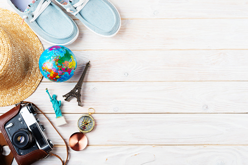 Travel planning simple background of compass, film camera, straw hat, moccasins, globe and souvenirs on white planks flat lay with copy-space