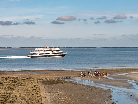 Mudflat hiking at low water and ferry in Wittdun channel, Amrum island, North Frisia, Schleswig-Holstein, Germany